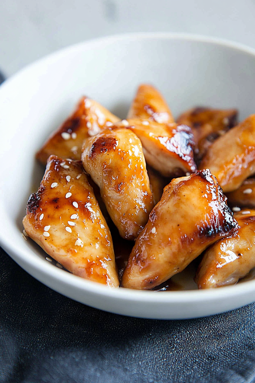 Tender glazed chicken served in a bowl with sesame seeds and extra sauce