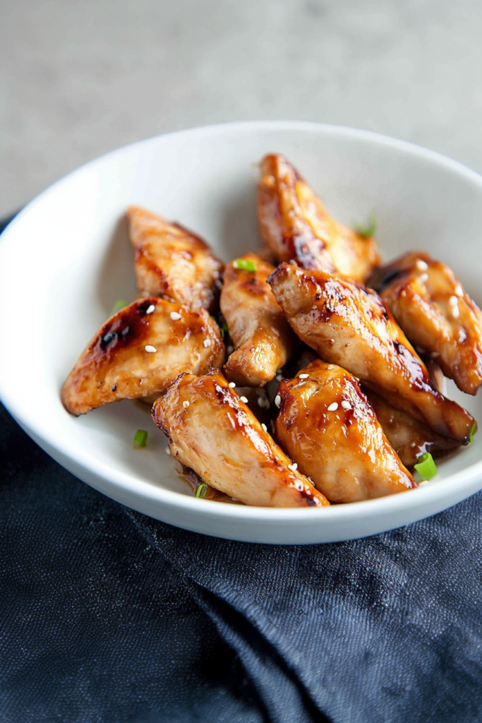 Glazed teriyaki chicken pieces sprinkled with sesame seeds in a white bowl