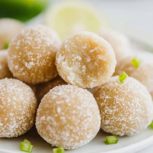 Light golden dessert balls covered in sugar, presented with vibrant lime accents.