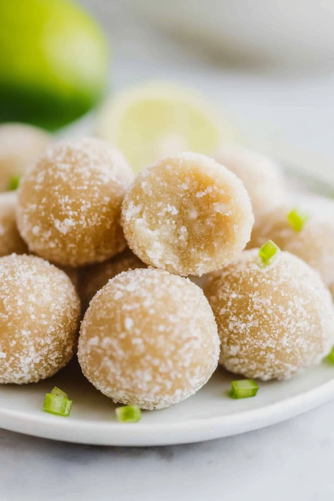 Light golden dessert balls covered in sugar, presented with vibrant lime accents.