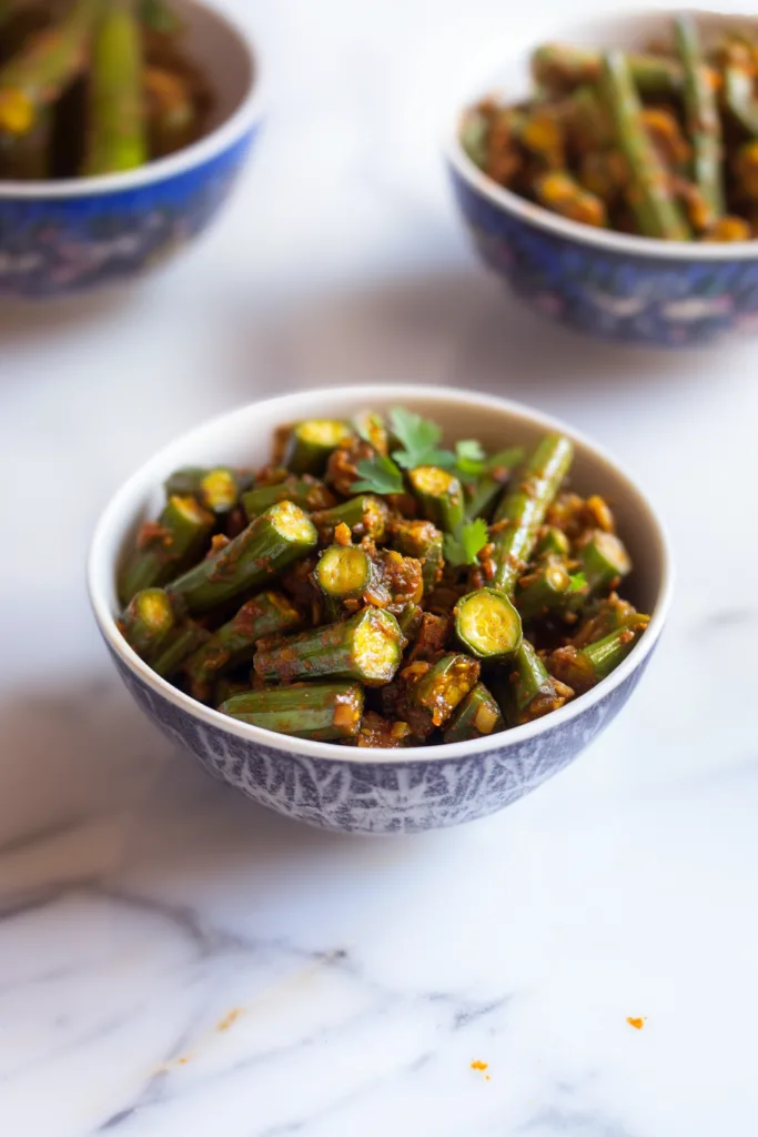 Bowl of sautรฉed okra coated in a spiced tomato masala with fresh cilantro garnish.
