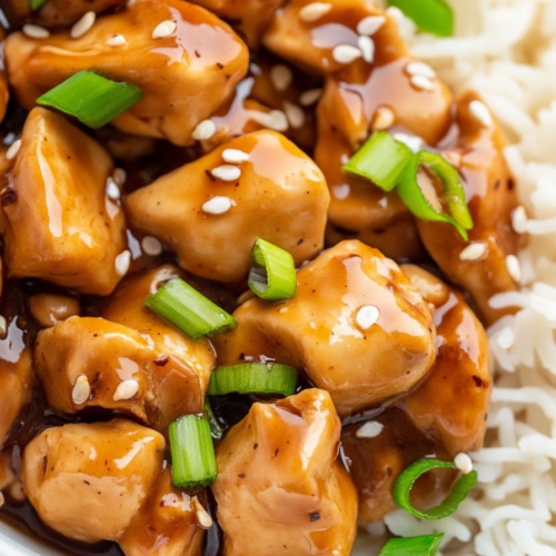 Close-up of tender chicken bites coated in a glossy savory sauce with fresh scallion garnish