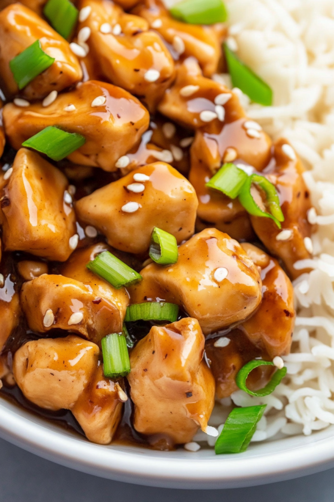 Close-up of tender chicken bites coated in a glossy savory sauce with fresh scallion garnish