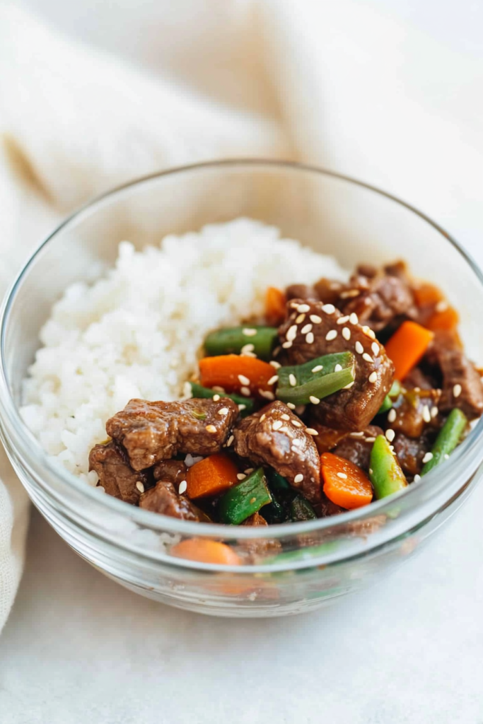 Glossy beef strips with carrots and green beans sprinkled with sesame seeds, ready to eat