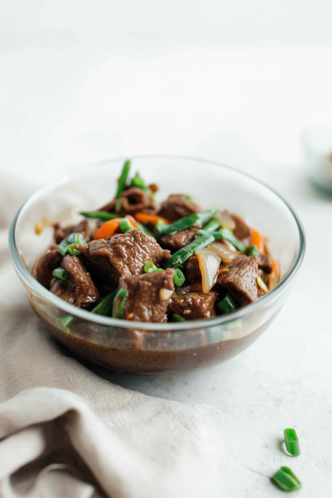 Tender beef strips in a glossy savory sauce with green beans and carrots in a glass bowl.