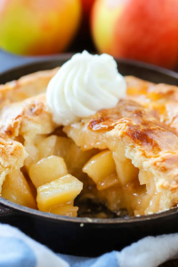 Golden baked apple pie in a cast iron skillet topped with a swirl of whipped cream