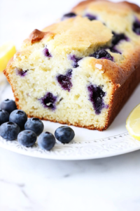 Freshly baked loaf cake with blueberries and a subtle lemon flavor, served with lemon slices on the side.