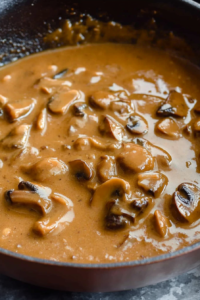Pan of rich, glossy mushroom gravy with tender slices of mushrooms in a creamy brown sauce.
