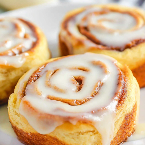 White plate holding iced cinnamon pastries, with a blurred coffee cup in the background.