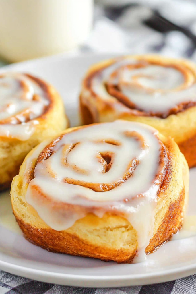 White plate holding iced cinnamon pastries, with a blurred coffee cup in the background.