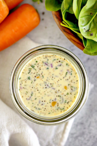 Glass jar of creamy herb dressing with specks of seasoning, placed beside a halved lemon.