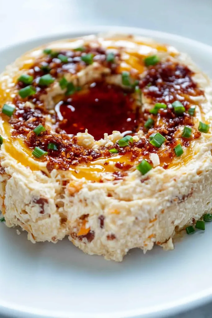 Cheese spread presented on a white plate, creamy texture highlighted by colorful garnishes and bold sauce.