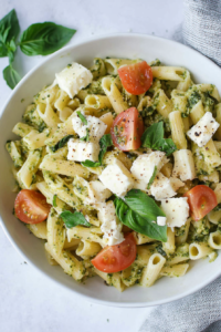 Freshly prepared pasta salad featuring pesto-coated penne, juicy tomatoes, and cubes of soft white cheese.