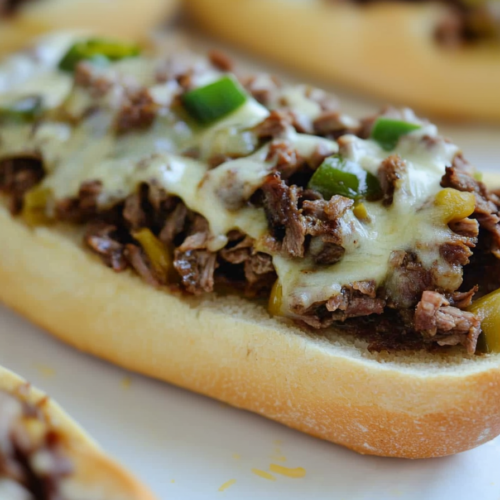 Open-faced toasted roll covered with tender steak pieces and melted cheese garnish.
