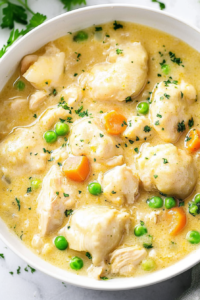 Close-up of homemade dumplings and chicken in a thick, creamy gravy with herbs