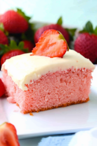 Close-up of frosted cake slice with fresh strawberries in the background.