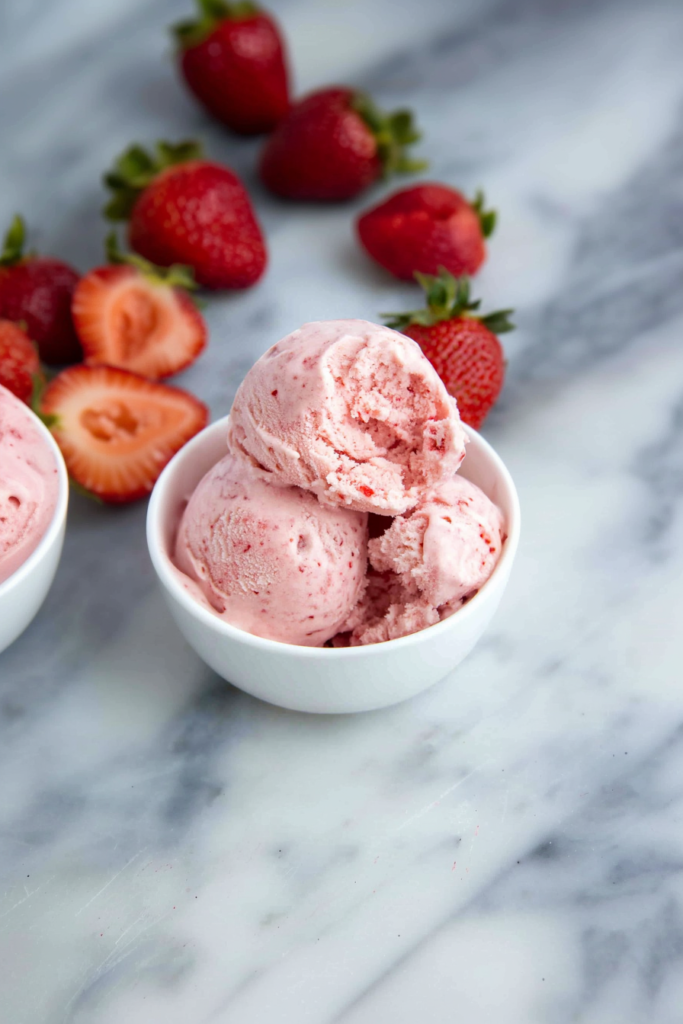 Scoops of creamy pink strawberry ice cream served in a white bowl.