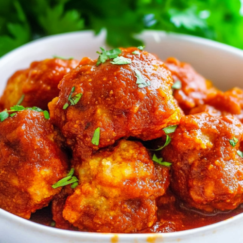 White bowl filled with tender meatballs coated in thick, red sauce for a hearty presentation.