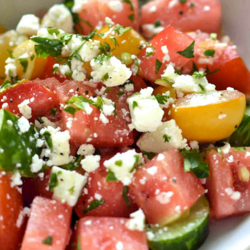 Fresh watermelon and tomato salad topped with crumbled cheese and herbs