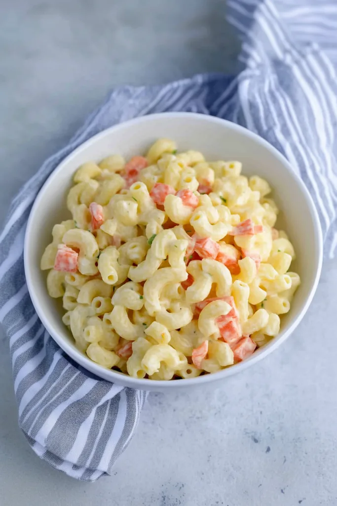 White bowl of macaroni salad resting on a striped cloth background.