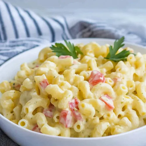 Creamy macaroni pasta mixed with red bell pepper pieces and parsley garnish.