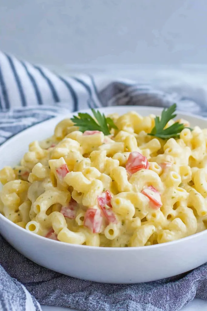 Creamy macaroni pasta mixed with red bell pepper pieces and parsley garnish.