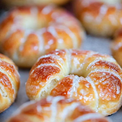 Freshly baked ringโshaped pastries with light glaze, soft texture highlighted by cracked tops.