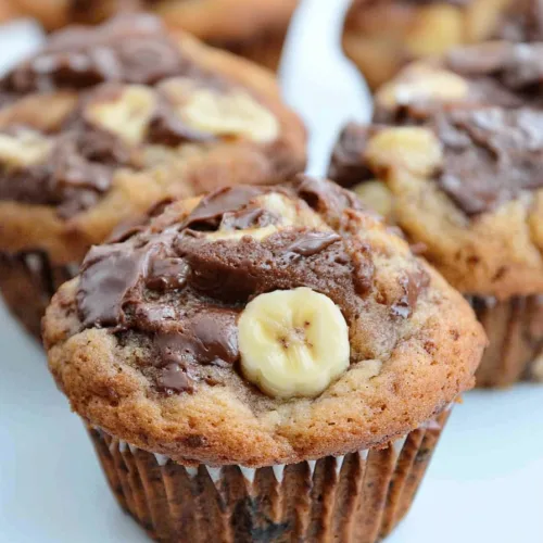 Batch of warm muffins arranged on a white surface, highlighting rich chocolate topping.