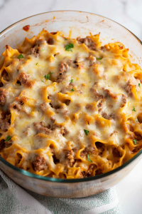 Comforting baked pasta dish with visible layers of noodles, beef, and sauce beneath a cheesy crust.