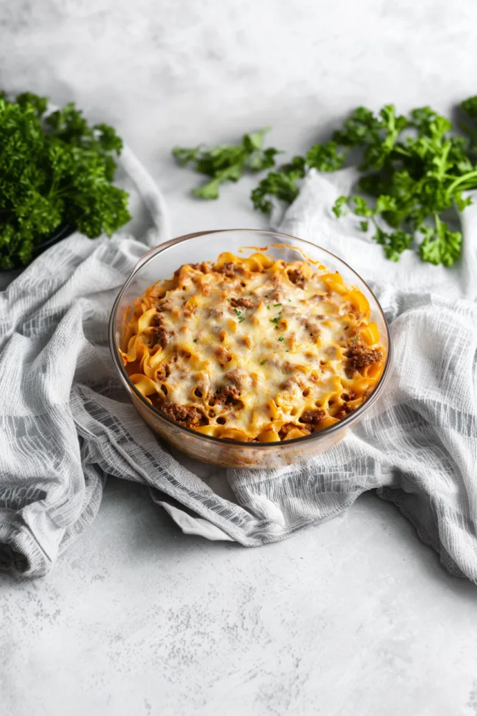 Golden-brown baked pasta topped with melted cheese and fresh parsley in a glass casserole dish.