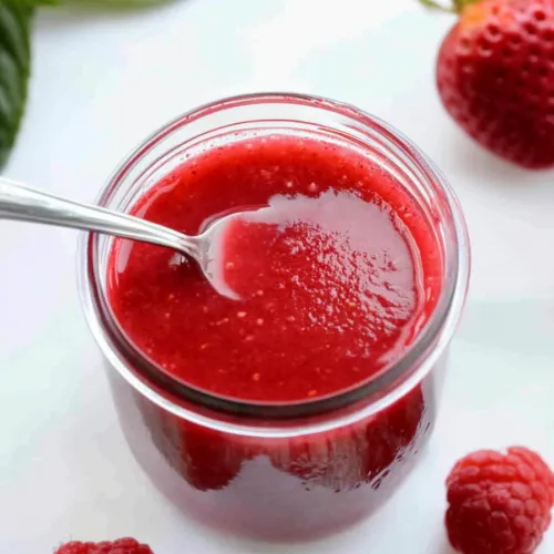 Glossy red sauce served in a white bowl with a silver spoon resting inside.