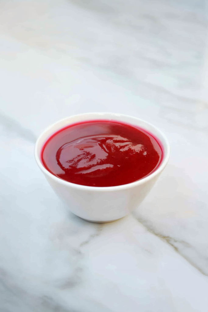 Smooth, glossy red sauce served in a small white bowl on a marble surface.