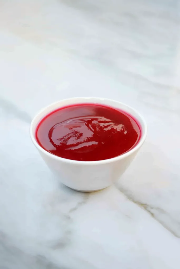 Smooth, glossy red sauce served in a small white bowl on a marble surface.