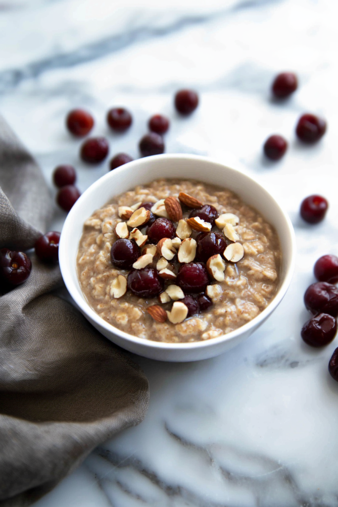 Creamy bowl of oatmeal topped with dark red cherries and chopped nuts.
