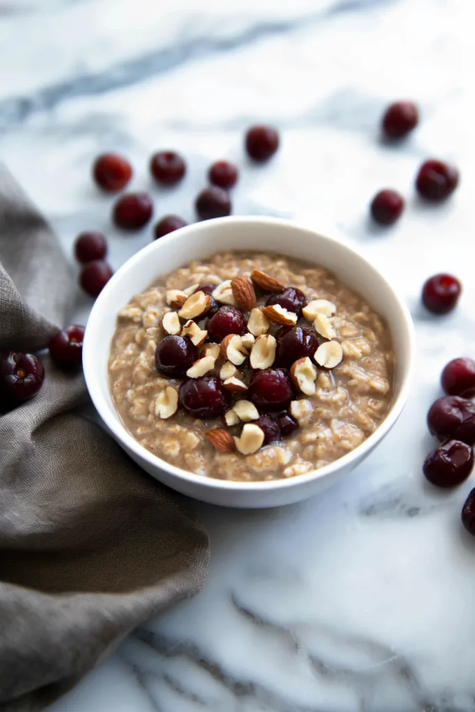 Creamy bowl of oatmeal topped with dark red cherries and chopped nuts.