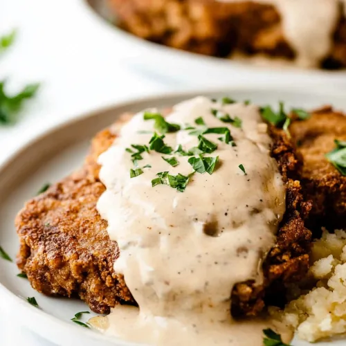 Golden fried steak smothered in rich pepper gravy on a plate with fluffy mashed potatoes.