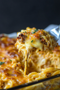 Serving spoon lifting a portion of cheesy pasta bake from the dish.