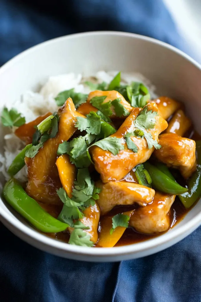 Close-up of stir-fried chicken served with colorful vegetables and steamed rice.