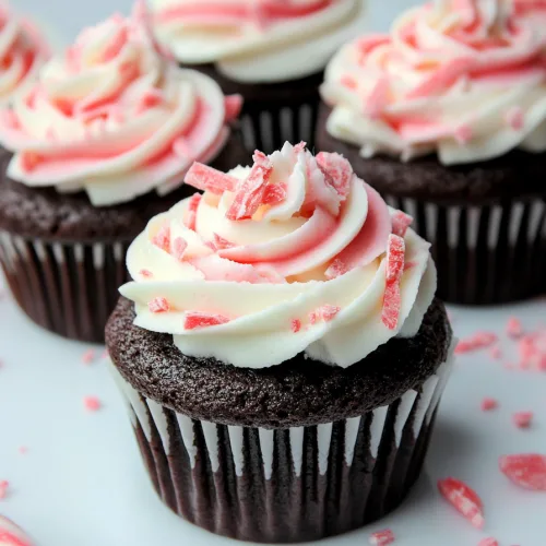 Dark chocolate cupcakes topped with swirls of pink and white frosting, sprinkled with crushed peppermint.
