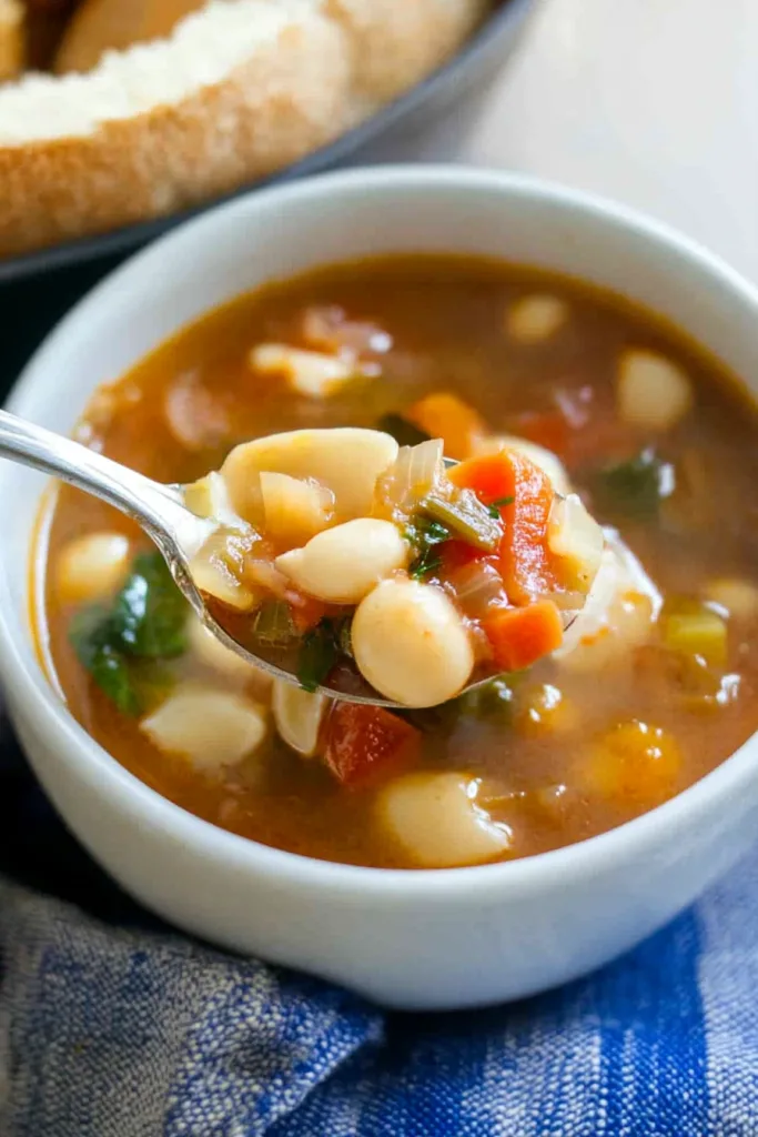 Spoon lifting a colorful mix of vegetables and broth above the bowl.