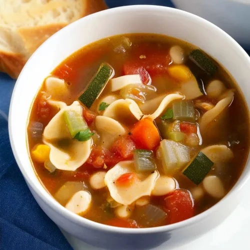 Comforting soup served with bread in the background on a blue cloth.