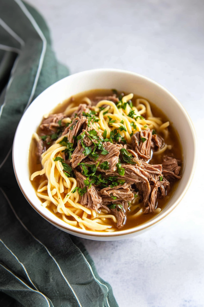 Comfort food dinner with slow-cooked beef, savory gravy, and soft noodles in a bowl