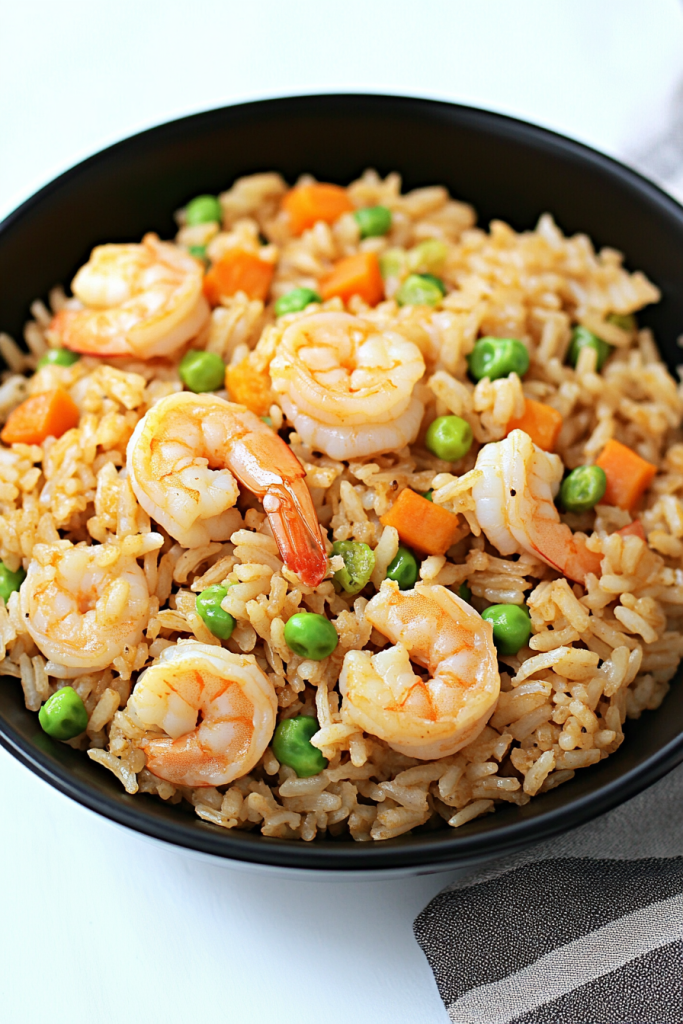 Golden fried rice topped with juicy shrimp, green peas, and diced carrots in a black serving bowl