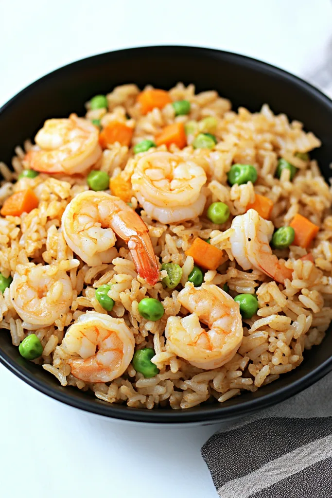 Golden fried rice topped with juicy shrimp, green peas, and diced carrots in a black serving bowl
