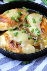 Savory cheesy chicken topped with caramelized onion slices and fresh green onions in a rustic pan.