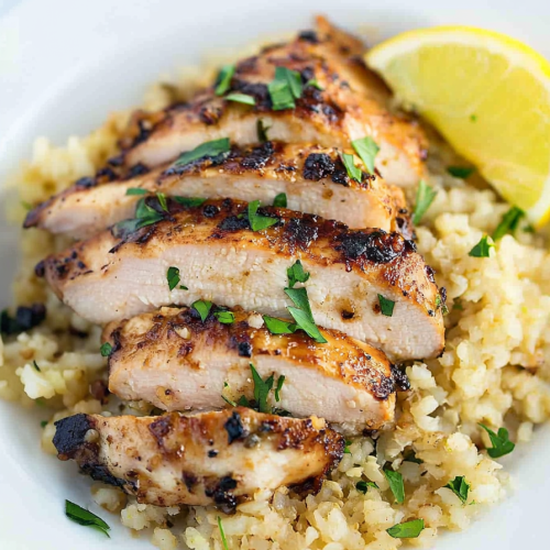 Savory chicken served on a white plate with parmesan cauliflower rice and sprinkled parsley.