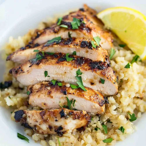 Savory chicken served on a white plate with parmesan cauliflower rice and sprinkled parsley.