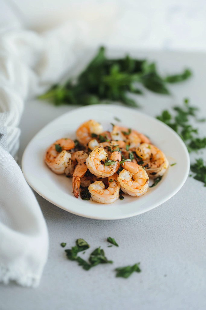 Juicy grilled shrimp arranged neatly on a white plate, garnished with chopped parsley.