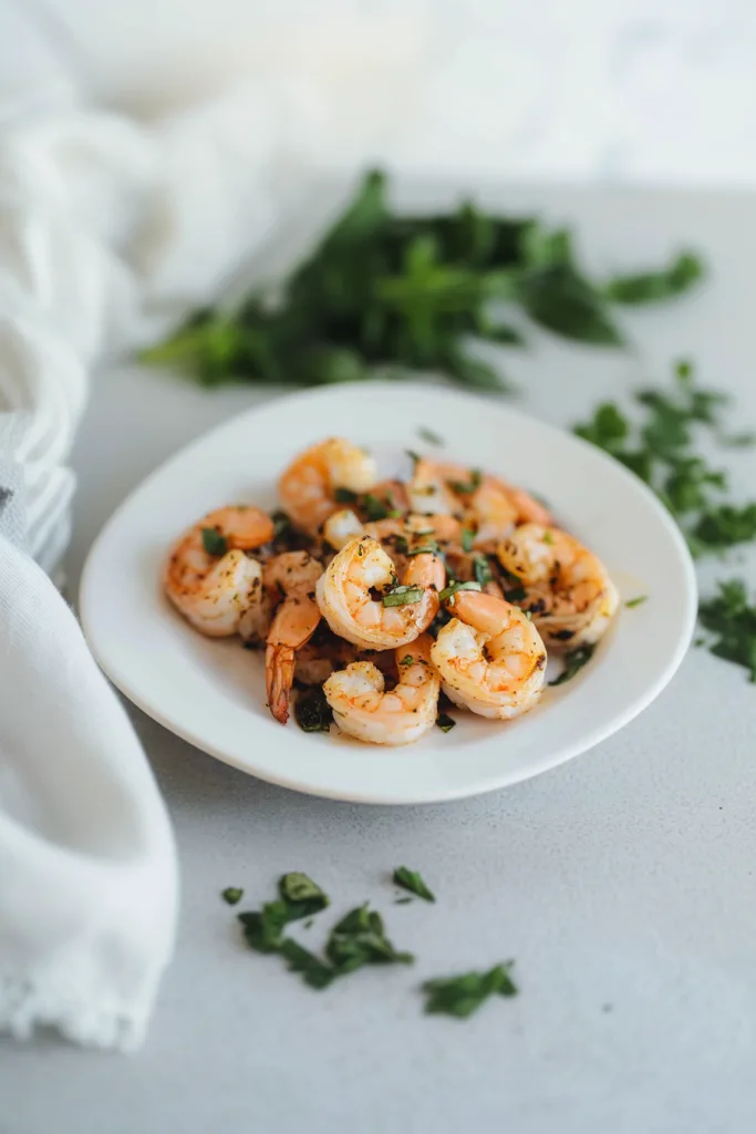 Juicy grilled shrimp arranged neatly on a white plate, garnished with chopped parsley.
