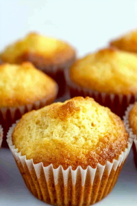 Freshly baked golden muffins in white paper liners, with domed tops and crisp edges.